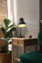 Photo of Wooden side table with glass of water, lamp and glasses indoors