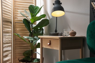 Photo of Wooden side table with glass of water, lamp and glasses indoors
