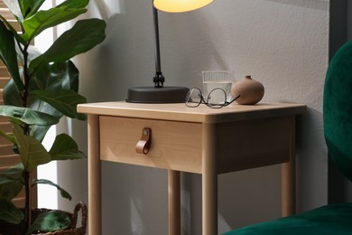 Photo of Wooden side table with glass of water, lamp and glasses indoors, closeup