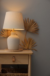 Photo of Stylish wooden side table with lamp near light wall at home