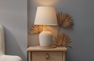Photo of Stylish wooden side table with lamp near light wall at home