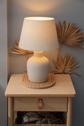Photo of Stylish wooden side table with lamp near light wall at home