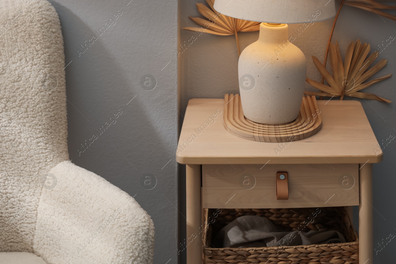 Stylish wooden side table with lamp near armchair at home, closeup Photo of Stylish wooden side table with lamp near armchair at home, closeup