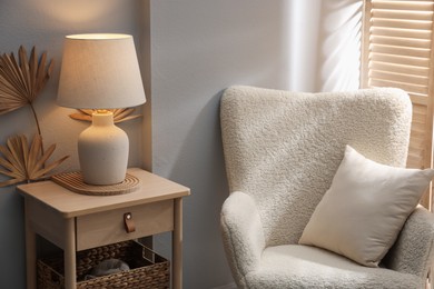 Photo of Stylish wooden side table with lamp near armchair at home