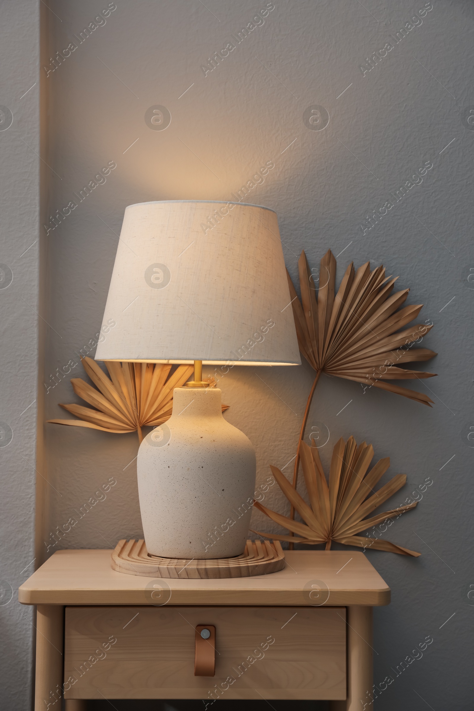 Stylish wooden side table with lamp near light wall at home Photo of Stylish wooden side table with lamp near light wall at home