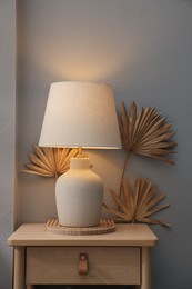 Photo of Stylish wooden side table with lamp near light wall at home