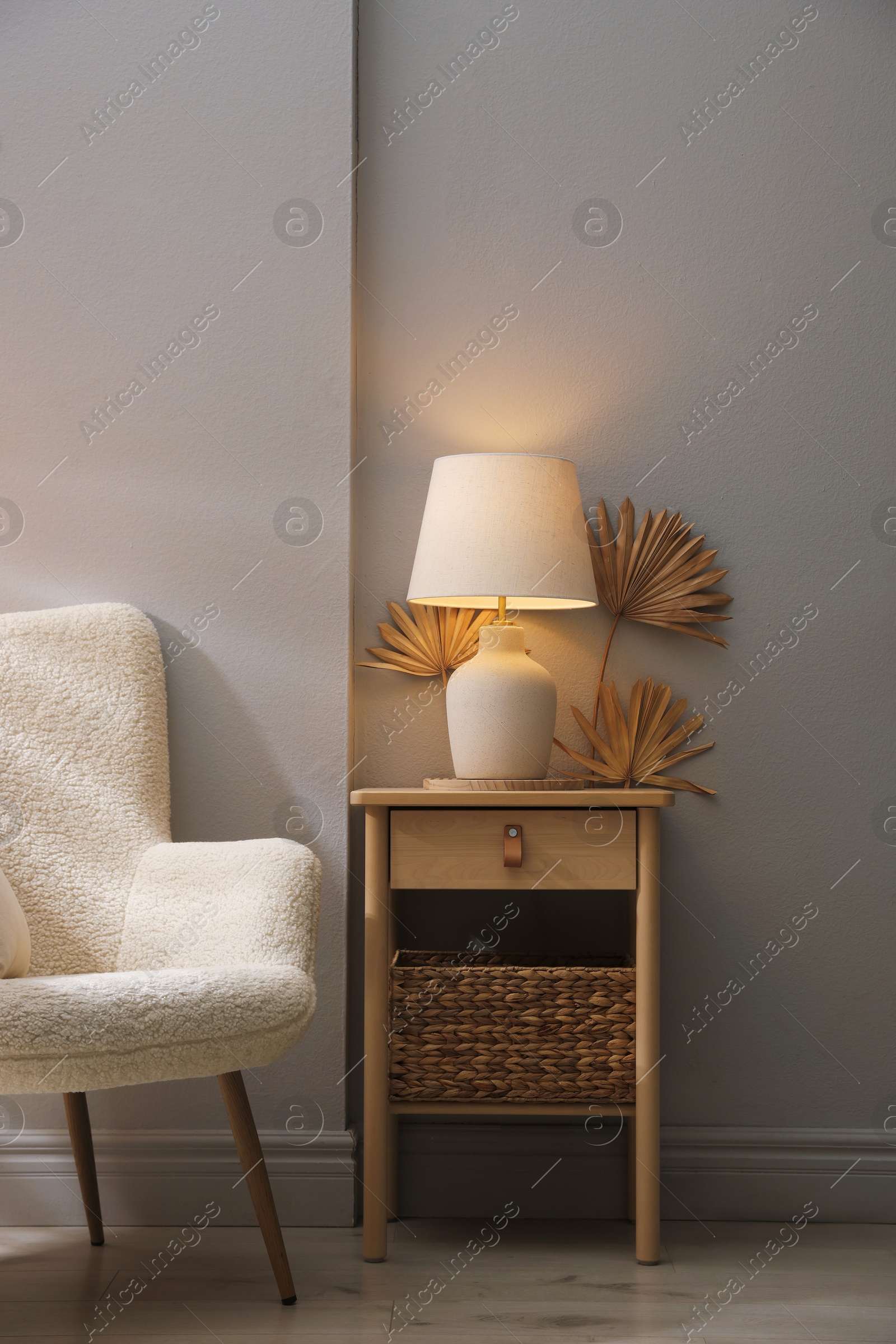 Stylish wooden side table with lamp near armchair at home Photo of Stylish wooden side table with lamp near armchair at home