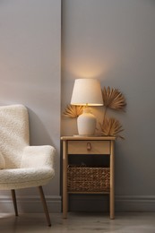 Photo of Stylish wooden side table with lamp near armchair at home
