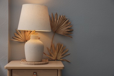 Photo of Stylish wooden side table with lamp near light wall at home. Space for text