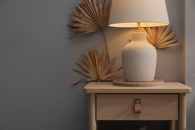 Photo of Stylish wooden side table with lamp near light wall at home, closeup. Space for text