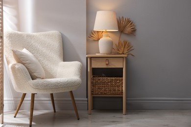 Photo of Stylish wooden side table with lamp near armchair at home