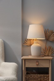 Photo of Stylish wooden side table with lamp near light wall at home