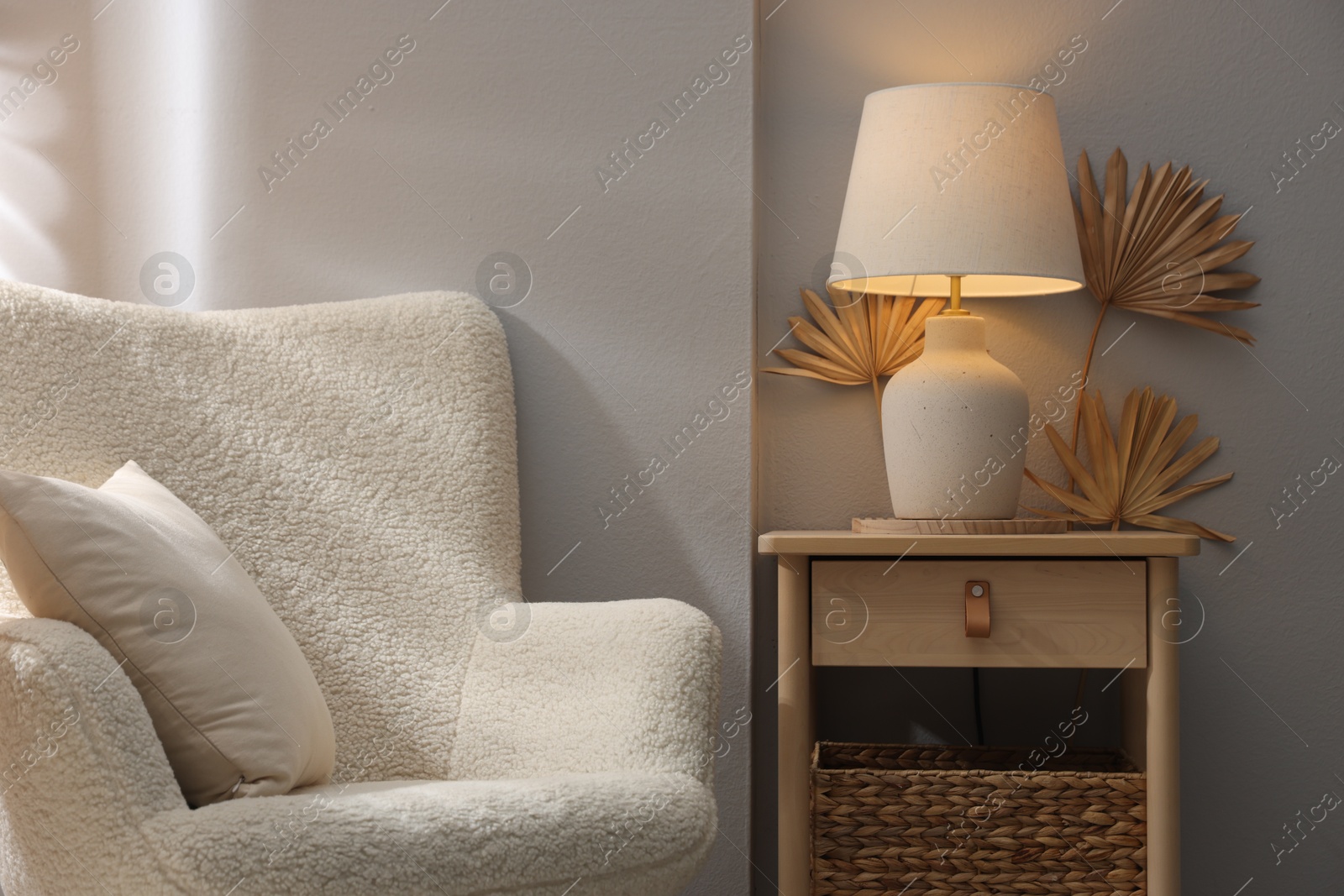 Stylish wooden side table with lamp near armchair at home Photo of Stylish wooden side table with lamp near armchair at home