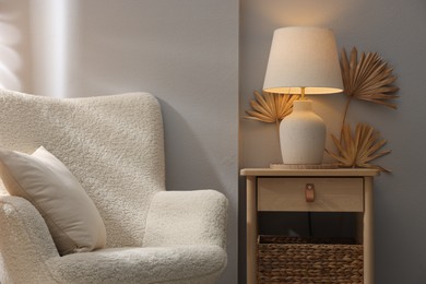 Photo of Stylish wooden side table with lamp near armchair at home