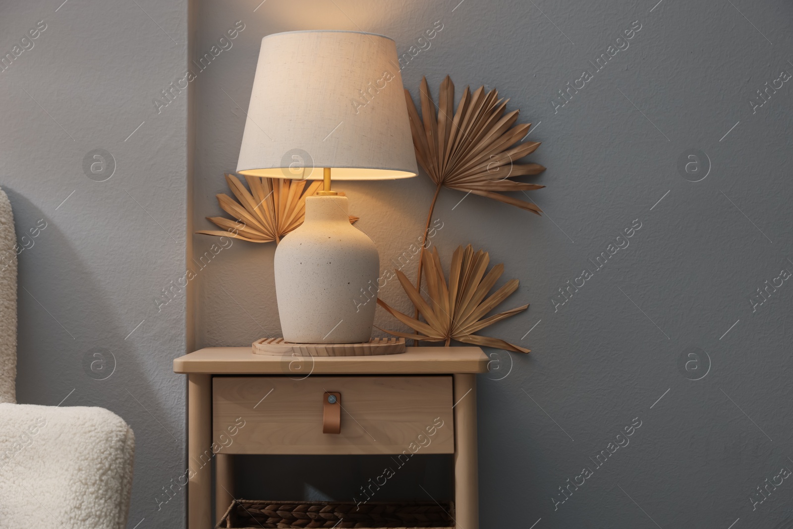 Stylish wooden side table with lamp near light wall at home. Space for text Photo of Stylish wooden side table with lamp near light wall at home. Space for text