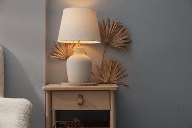 Photo of Stylish wooden side table with lamp near light wall at home. Space for text