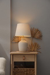 Photo of Stylish wooden side table with lamp near light wall at home