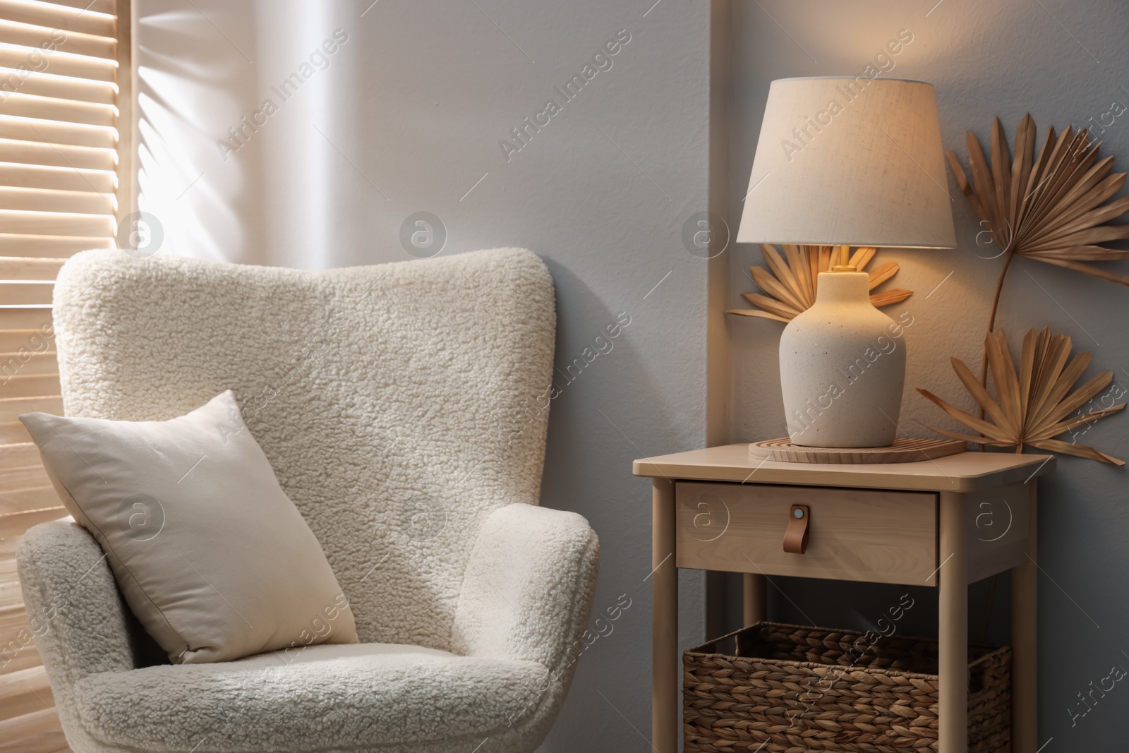 Stylish wooden side table with lamp near armchair at home Photo of Stylish wooden side table with lamp near armchair at home