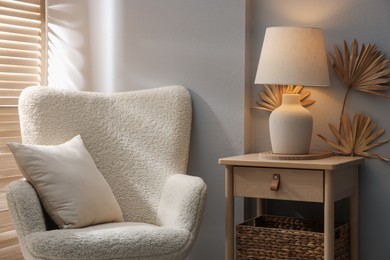 Photo of Stylish wooden side table with lamp near armchair at home
