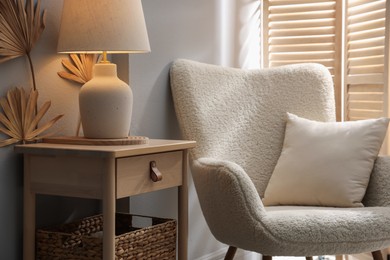 Photo of Stylish wooden side table with lamp near armchair at home