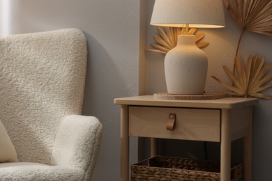 Photo of Stylish wooden side table with lamp near armchair at home, closeup