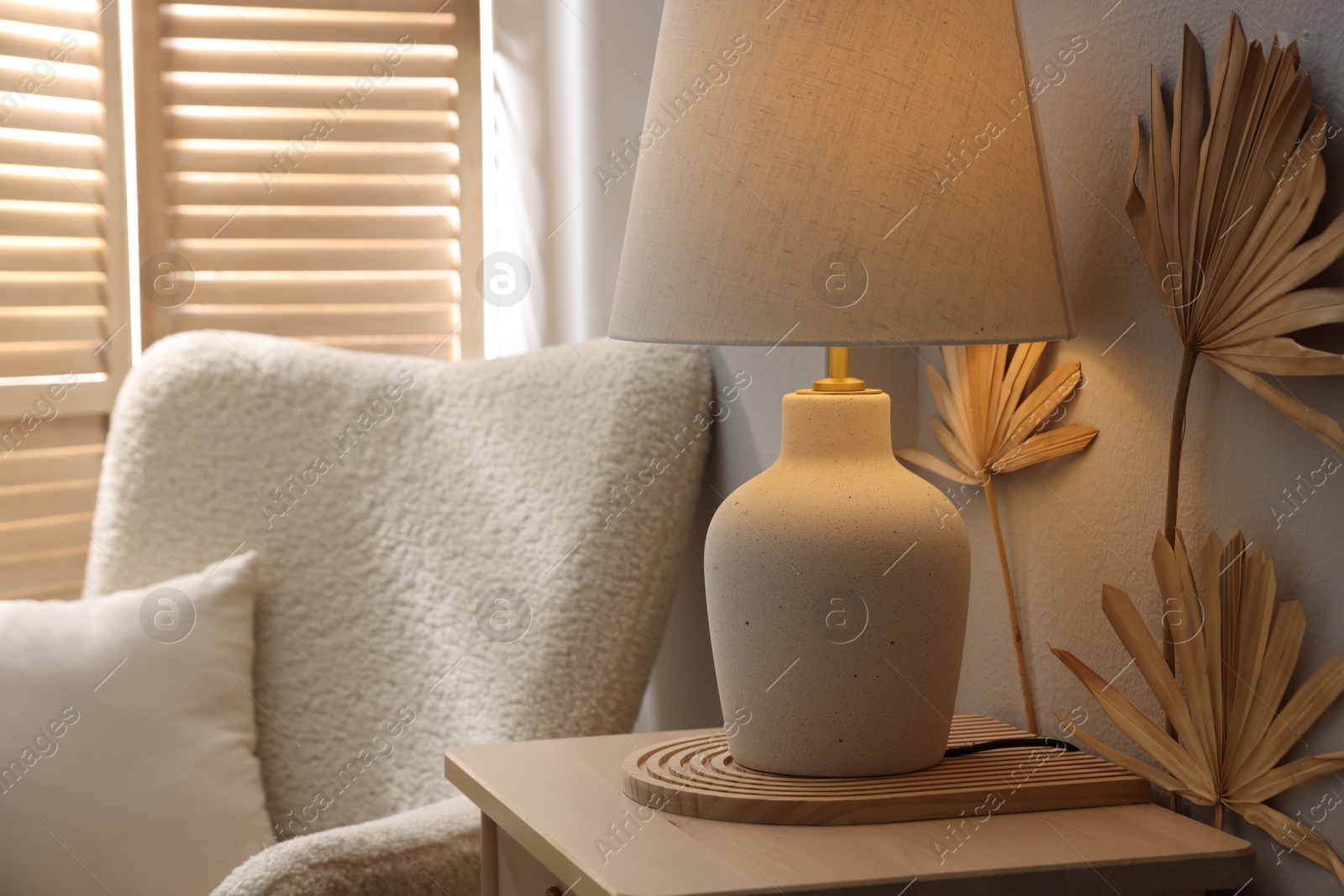 Stylish wooden side table with lamp near armchair at home, closeup Photo of Stylish wooden side table with lamp near armchair at home, closeup