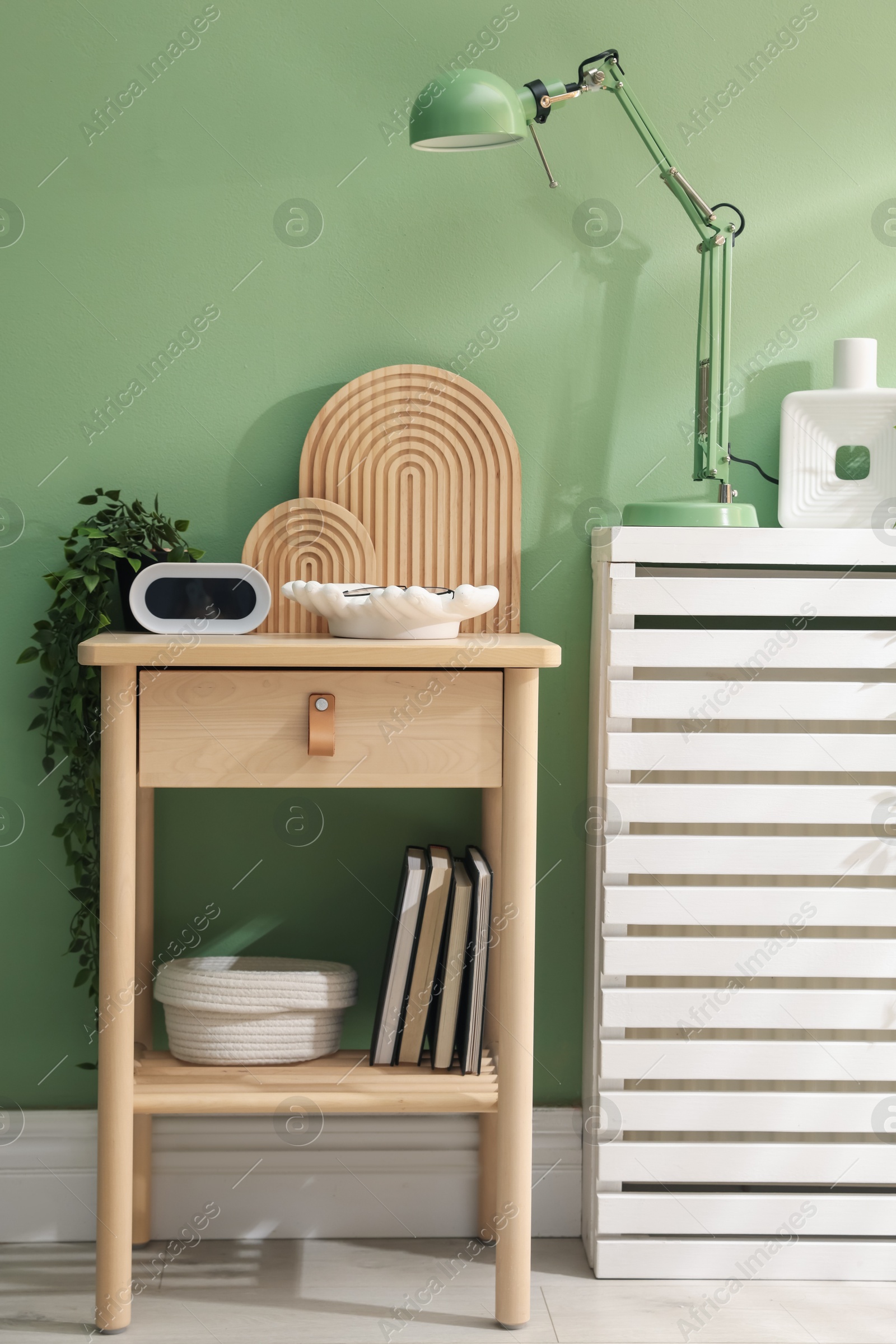 Wooden side table with stylish decor near green wall indoors Photo of Wooden side table with stylish decor near green wall indoors