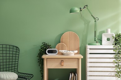 Photo of Wooden side table with stylish decor near green wall indoors
