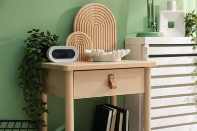 Photo of Wooden side table with stylish decor near green wall indoors, closeup