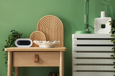 Photo of Wooden side table with stylish decor near green wall indoors