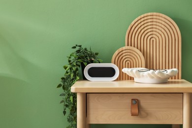 Photo of Wooden side table with stylish decor near green wall indoors, closeup. Space for text