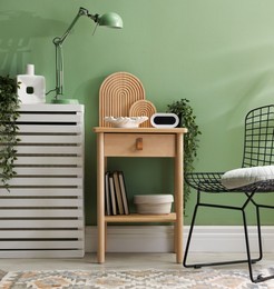 Photo of Wooden side table with stylish decor near green wall indoors