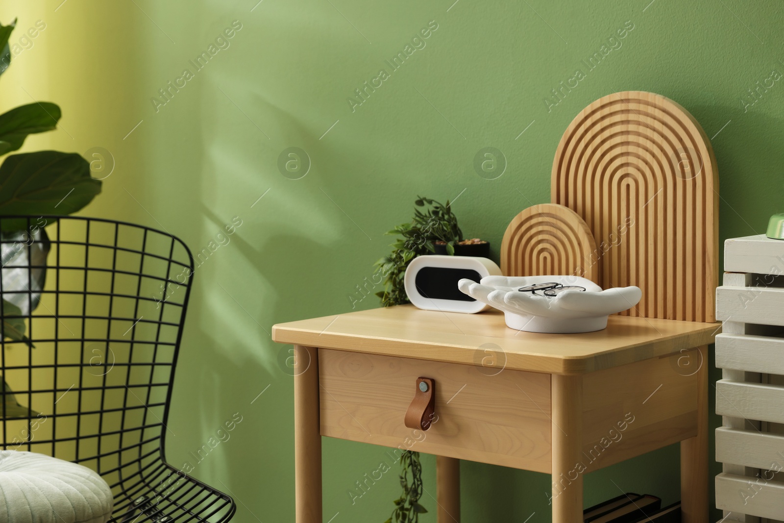 Wooden side table with stylish decor near green wall indoors, closeup Photo of Wooden side table with stylish decor near green wall indoors, closeup