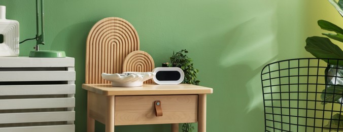 Photo of Wooden side table with stylish decor near green wall indoors, closeup