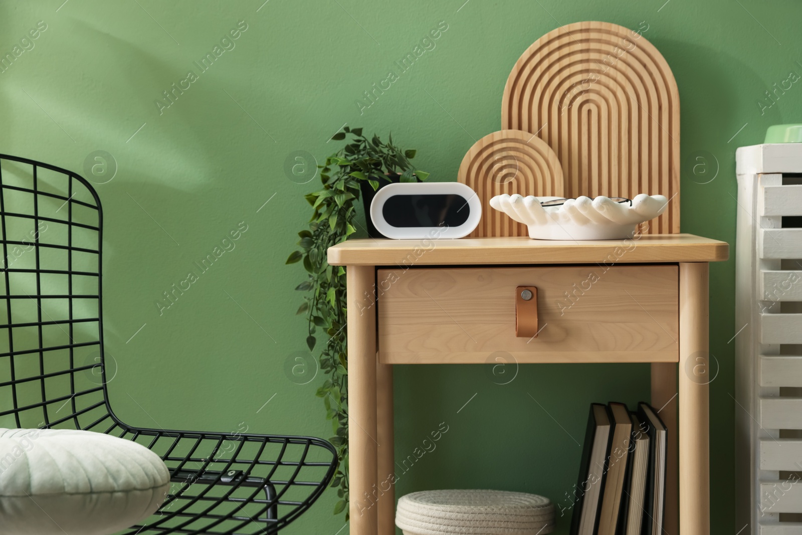 Wooden side table with stylish decor near green wall indoors, closeup Photo of Wooden side table with stylish decor near green wall indoors, closeup