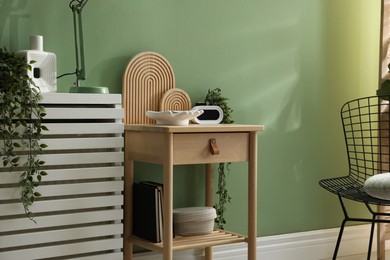 Photo of Wooden side table with stylish decor near green wall indoors