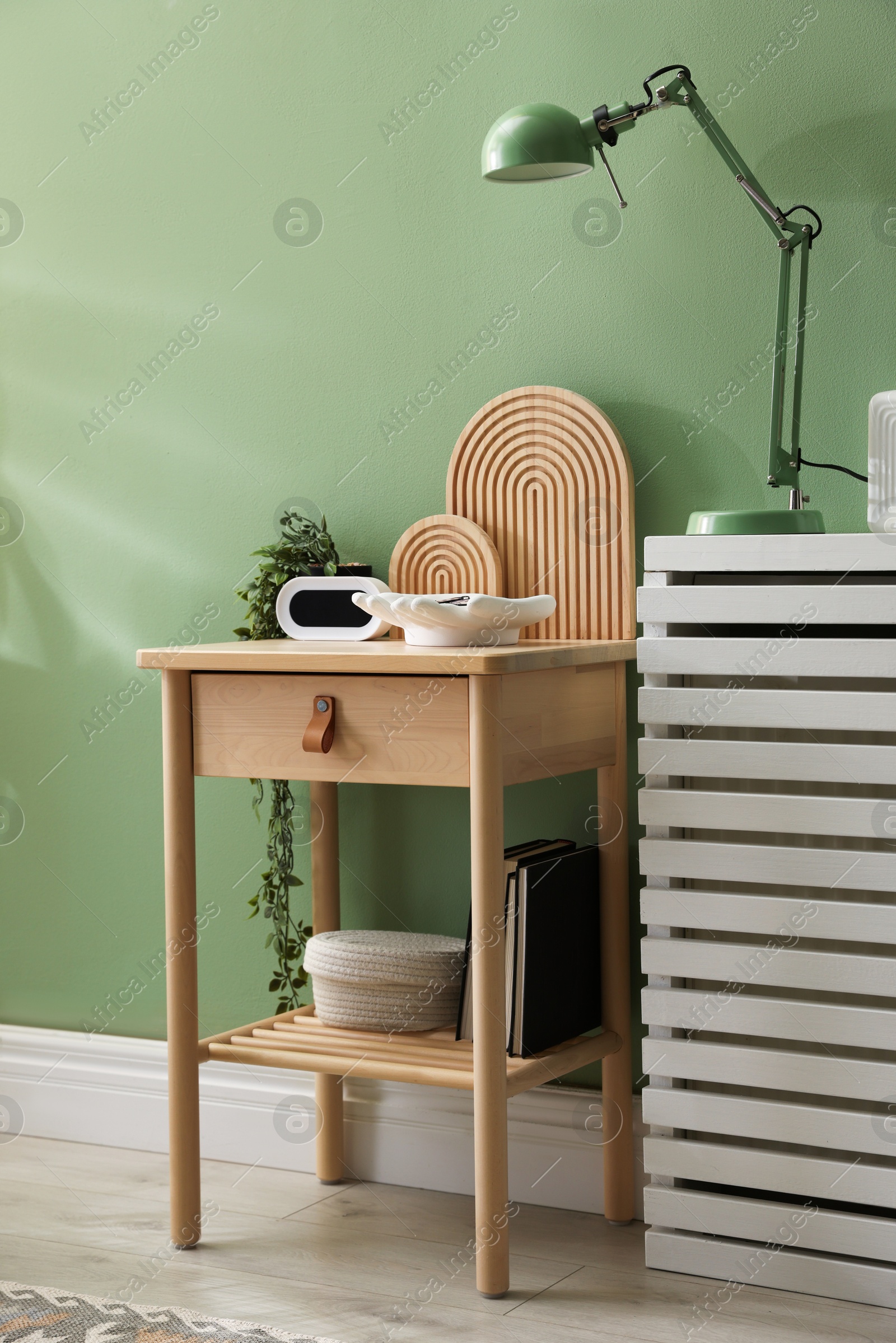Wooden side table with stylish decor near green wall indoors Photo of Wooden side table with stylish decor near green wall indoors
