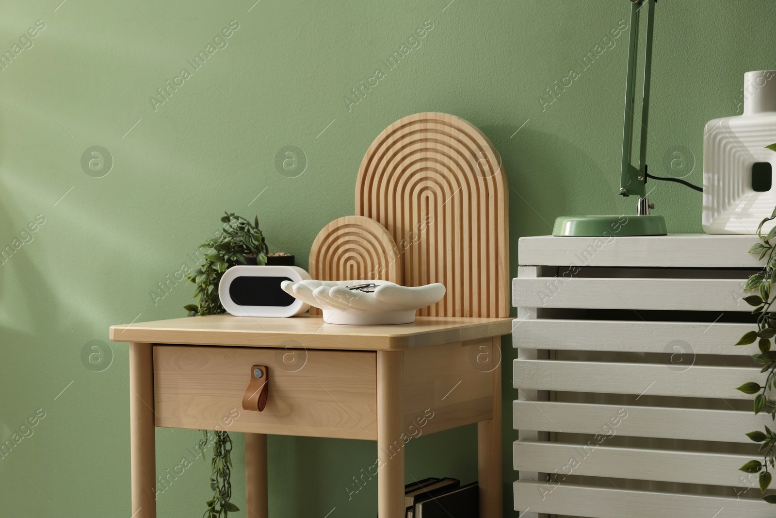 Wooden side table with stylish decor near green wall indoors, closeup Photo of Wooden side table with stylish decor near green wall indoors, closeup