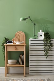 Photo of Wooden side table with stylish decor near green wall indoors