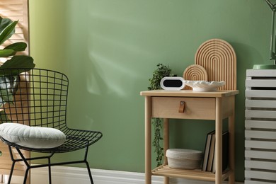 Photo of Wooden side table with stylish decor near green wall indoors