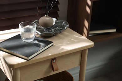 Photo of Wooden side table with glass of water, notebook and air reed diffuser indoors