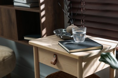 Photo of Wooden side table with glass of water, notebook and air reed diffuser indoors