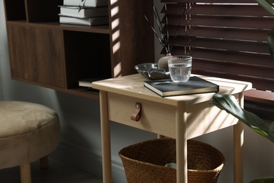Photo of Wooden side table with glass of water, notebook and air reed diffuser indoors