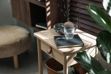 Photo of Wooden side table with glass of water, notebook and air reed diffuser indoors