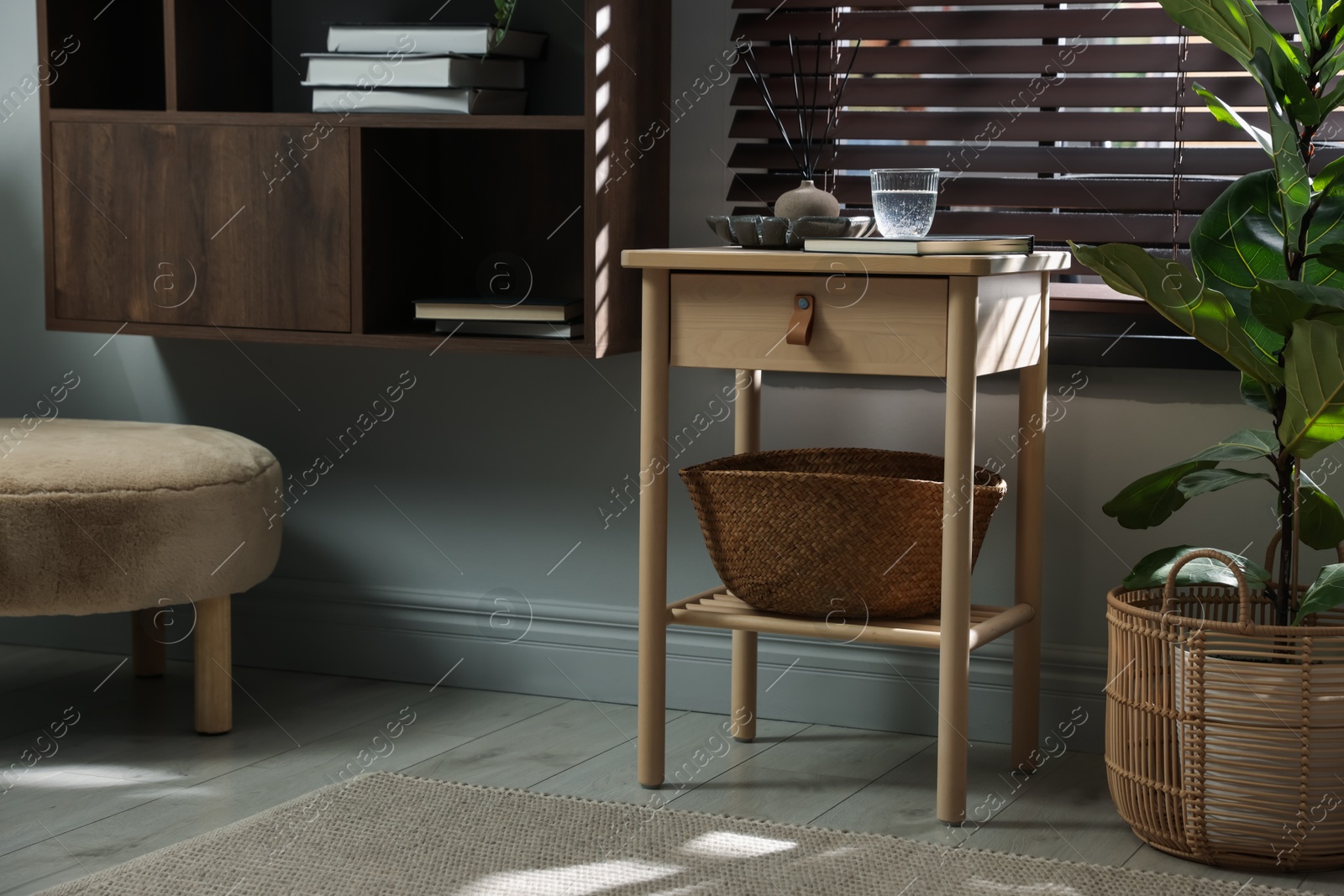 Wooden side table with glass of water, notebook, air reed diffuser and basket near window indoors Photo of Wooden side table with glass of water, notebook, air reed diffuser and basket near window indoors
