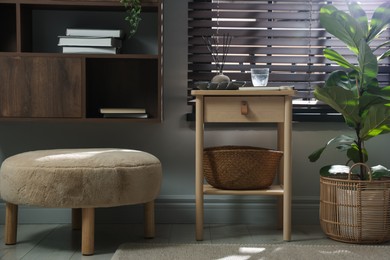 Photo of Wooden side table with glass of water, notebook, air reed diffuser and basket near window indoors