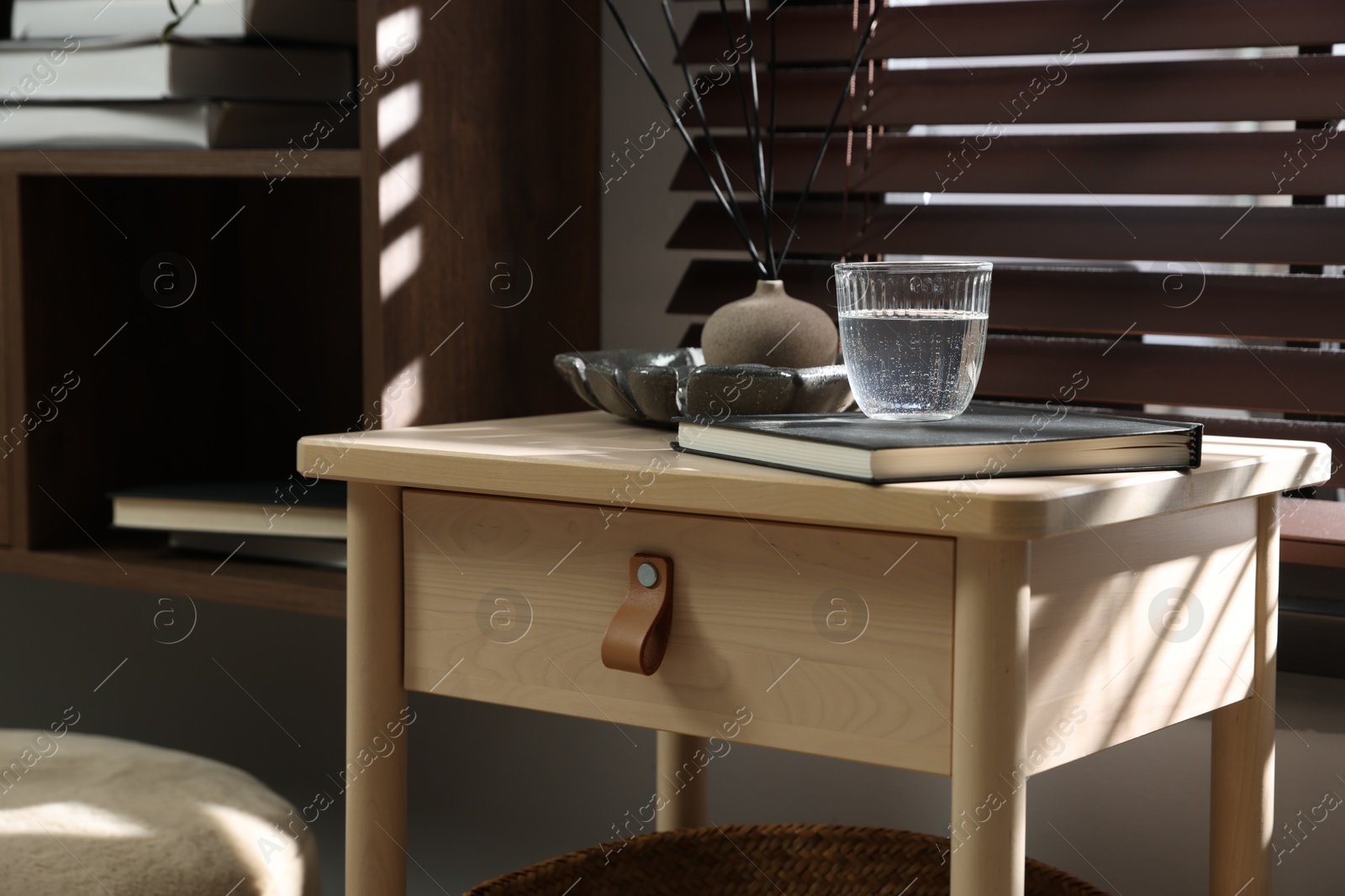 Wooden side table with glass of water, notebook and air reed diffuser indoors Photo of Wooden side table with glass of water, notebook and air reed diffuser indoors