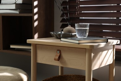 Photo of Wooden side table with glass of water, notebook and air reed diffuser indoors