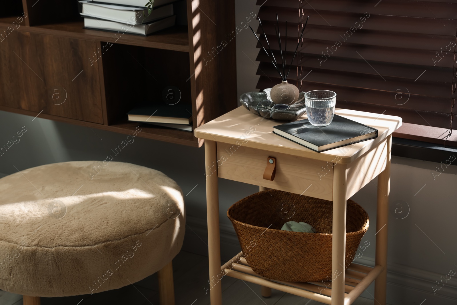 Wooden side table with glass of water, notebook, air reed diffuser and basket near window indoors Photo of Wooden side table with glass of water, notebook, air reed diffuser and basket near window indoors