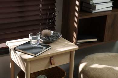 Photo of Wooden side table with glass of water, notebook and air reed diffuser indoors